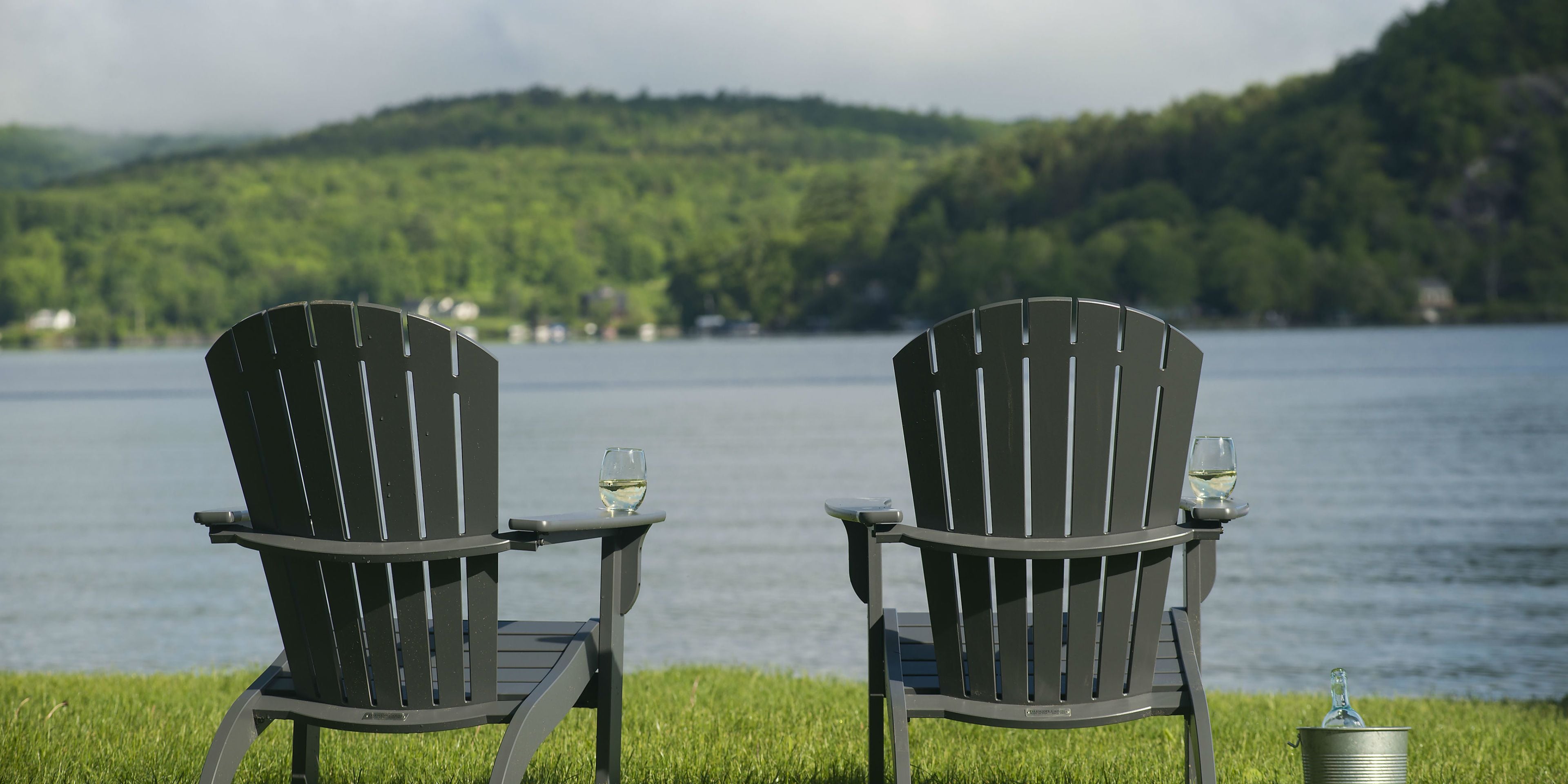 Dos sillas Adirondack mirando un lago con una ladera boscosa al fondo.
