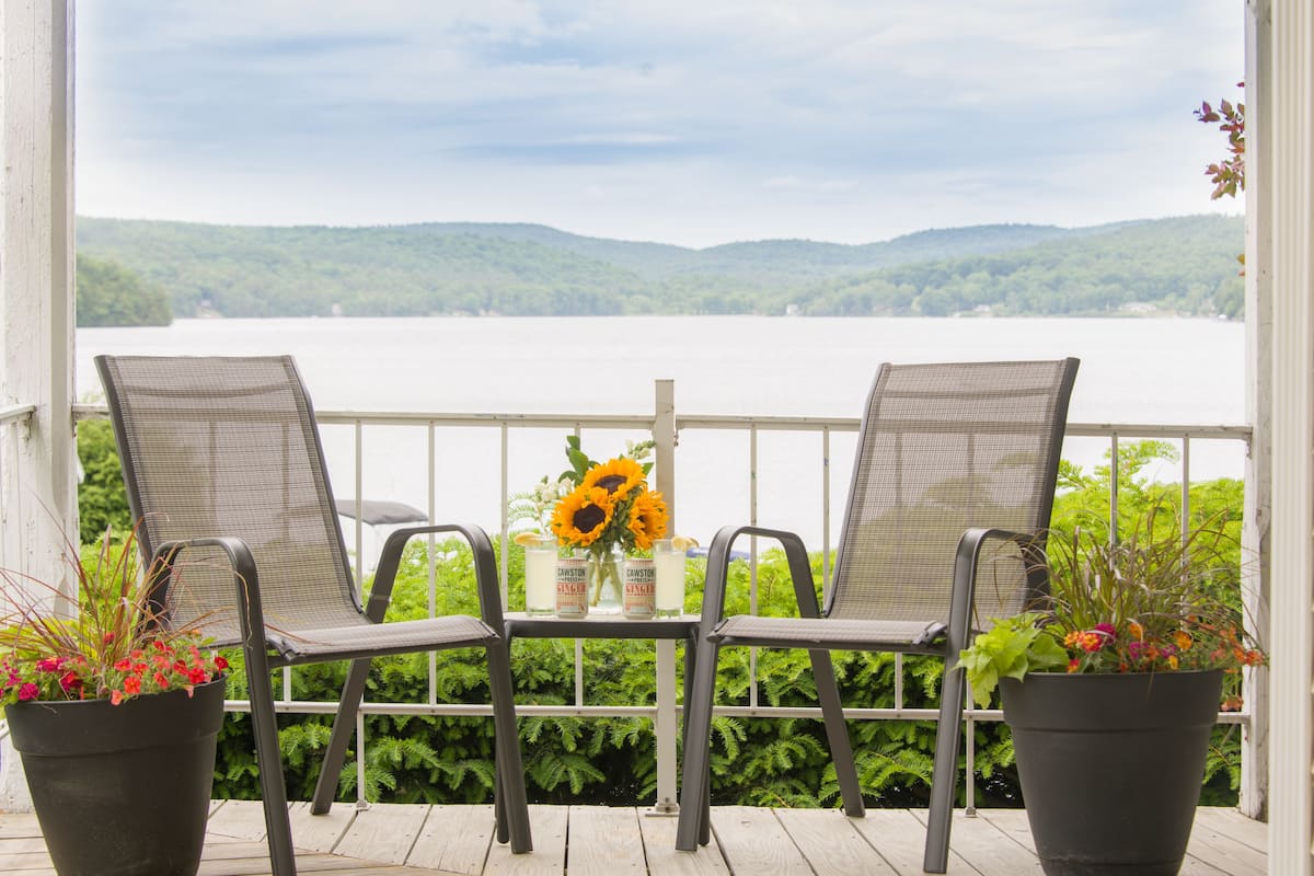 Un balcon avec deux chaises et une table, donnant sur un lac et des collines.