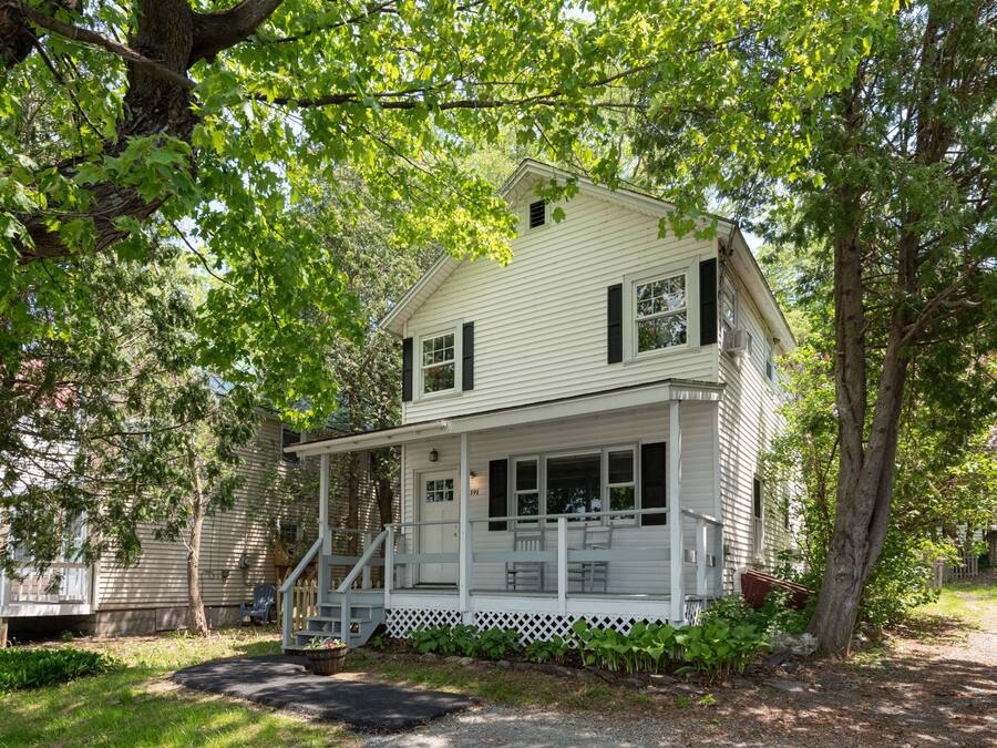 A two-story house with a porch, surrounded by trees and a well-maintained garden.
