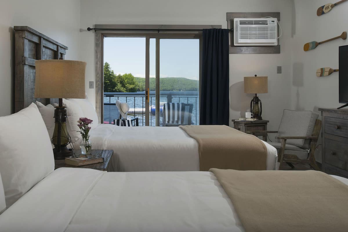 Une chambre d’hôtel avec deux lits, un bureau, une chaise, une lampe, une télévision et une vue sur le lac.