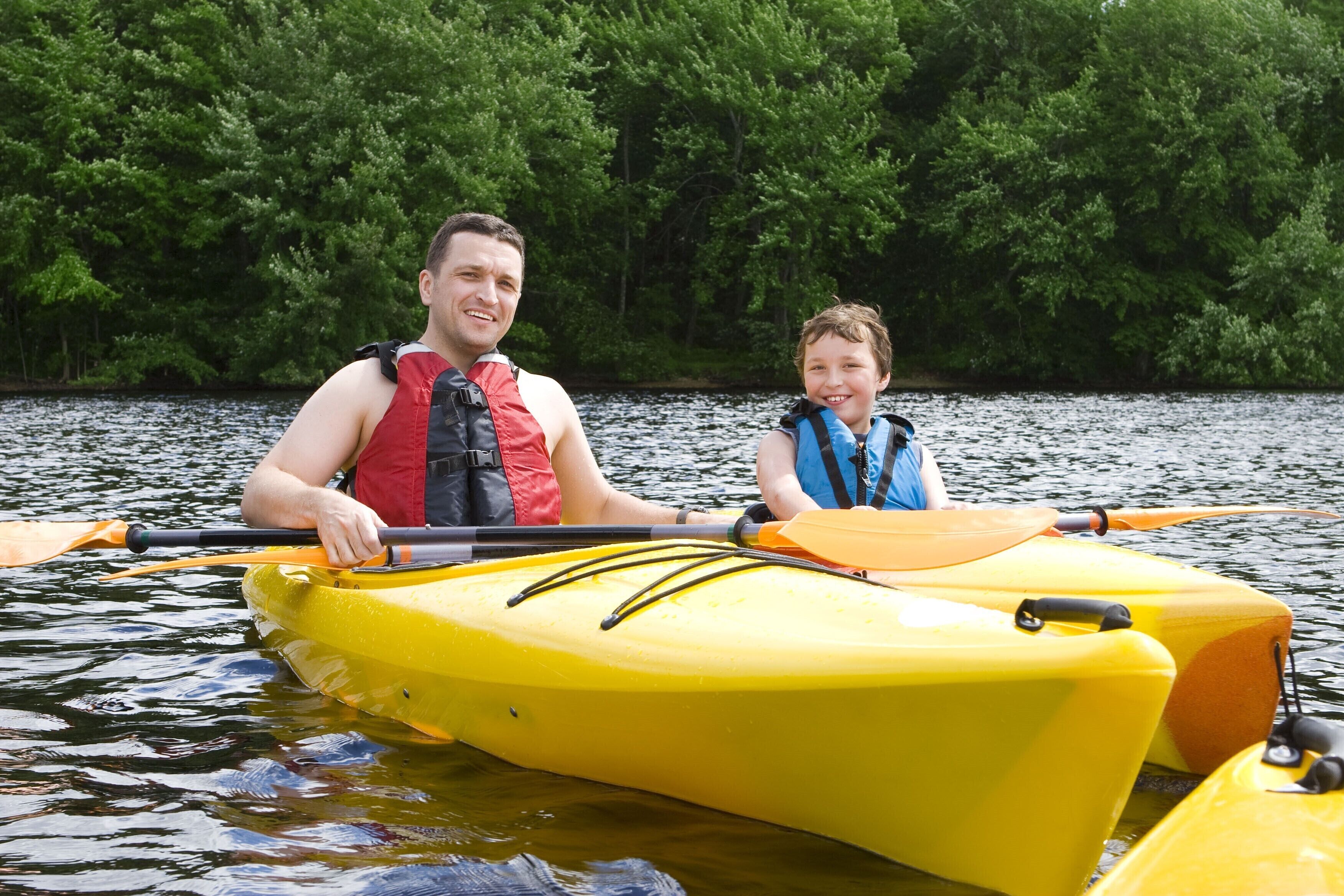 Deux personnes dans un kayak jaune sur une étendue d’eau calme, entourées d’une végétation verdoyante et luxuriante.