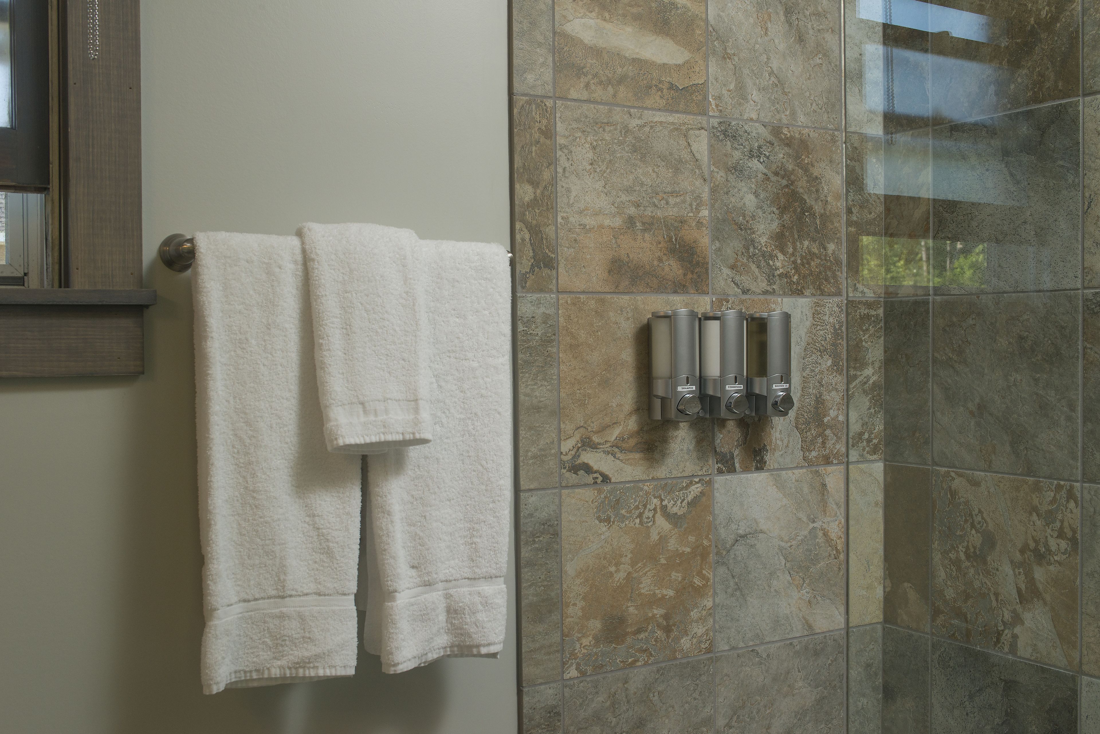 Un baño con zona de ducha, paredes revestidas de azulejos y un perchero con dos toallas.