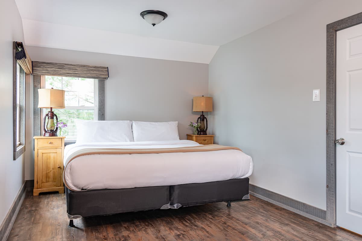 Une chambre à coucher avec un grand lit, deux tables de chevet avec des lampes, une fenêtre avec des stores et une porte.