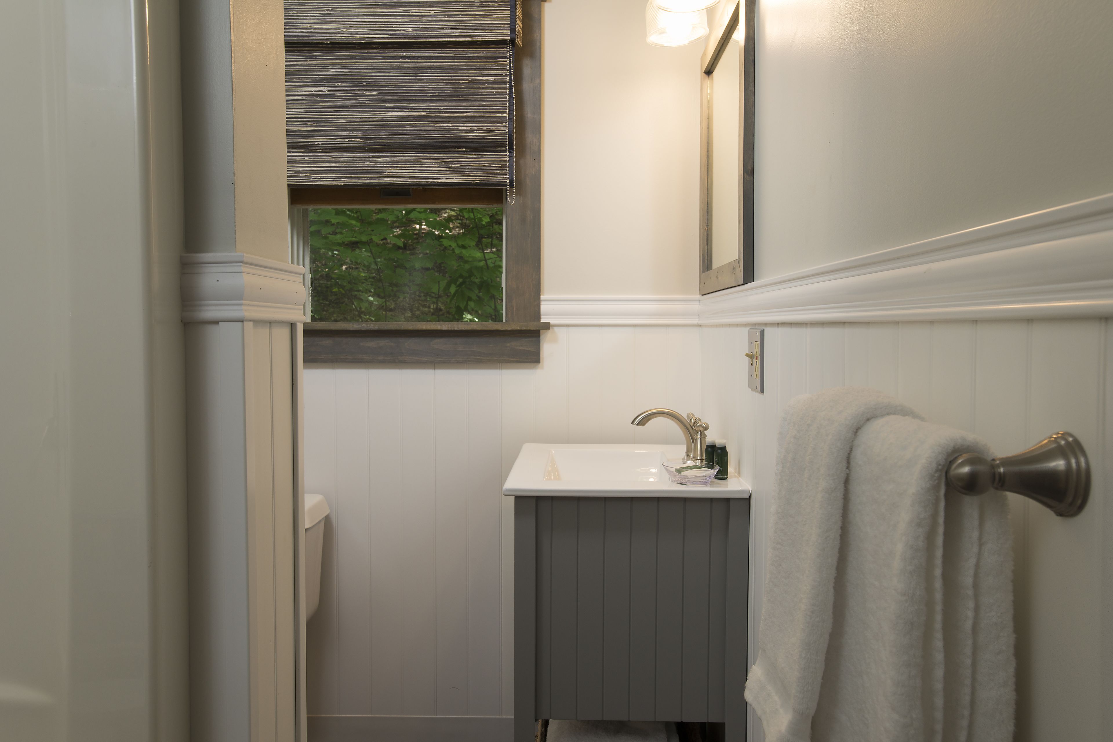 Un baño con lavamanos blanco, un perchero y una ventana con persianas.