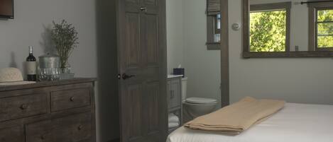 Een slaapkamer met een bed, een dressoir, een spiegel en een deur naar een badkamer.