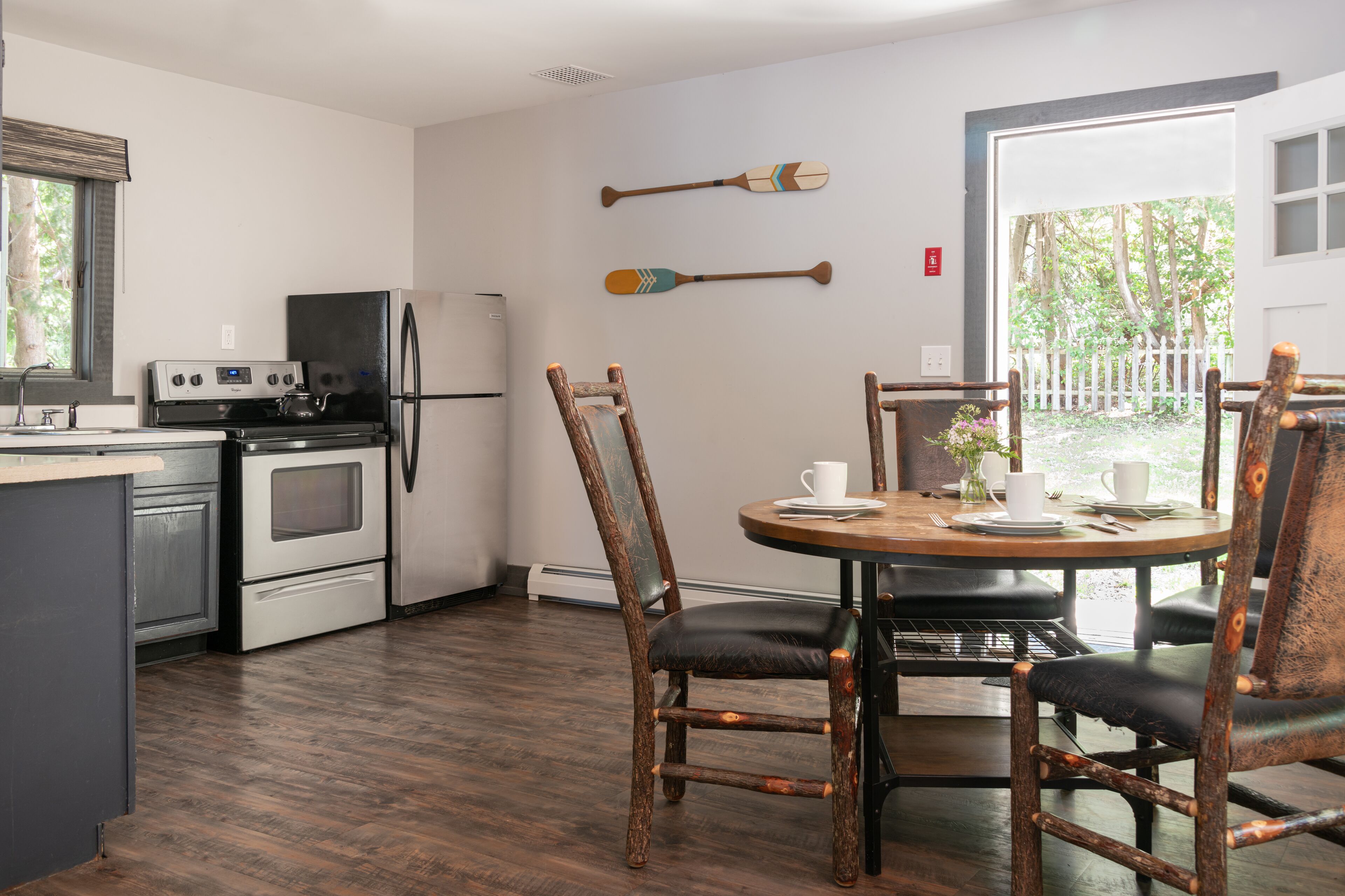 A kitchen with a stove, oven, and refrigerator. There is a dining table with chairs and a window with a view of trees.