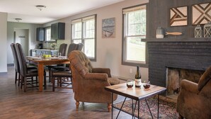 Un salón amplio con chimenea, un comedor con mesa y sillas de madera, y ventanas grandes que dejan entrar luz natural.