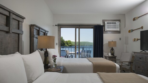 Habitación de hotel con dos camas, un ventanal con vistas al mar, un televisor y un escritorio con lámpara.