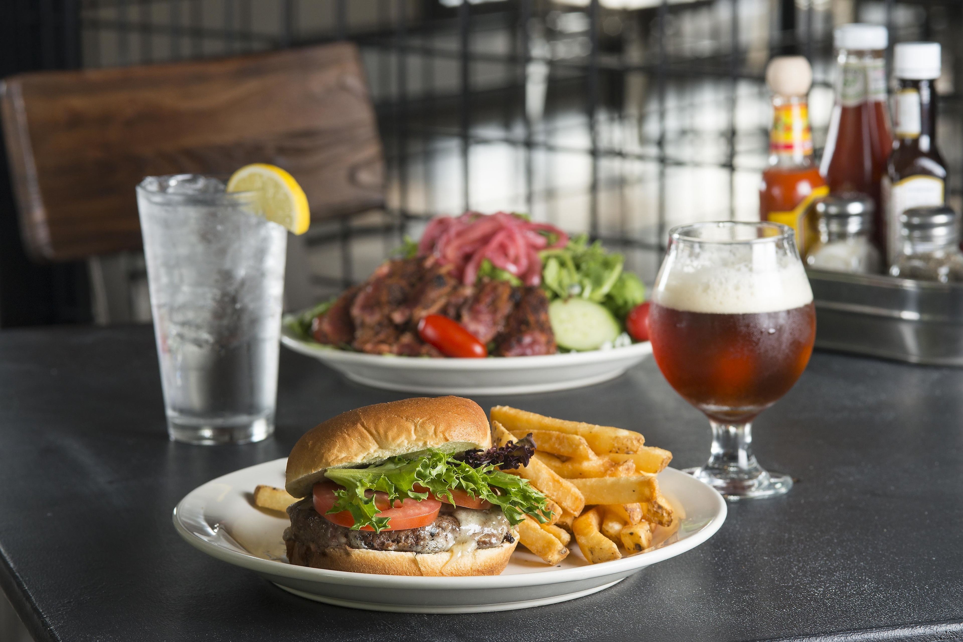 Un repas composé d’un hamburger, de frites et d’un verre de bière, le tout posé sur une table.