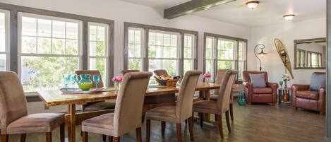 A dining area with a wooden table and chairs, large windows, and a ceiling with exposed beams.