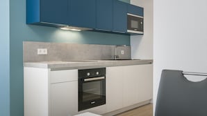 A modern kitchen with teal cabinets, a microwave, a sink, and a dining area with a plate of croissants and a cup of coffee. - Appartments Drei Morgen (Leinfelden-Echterdingen)