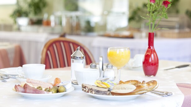 A breakfast table with a variety of foods, a glass of orange juice, and a vase of red flowers. - Appartments Drei Morgen (Leinfelden-Echterdingen)