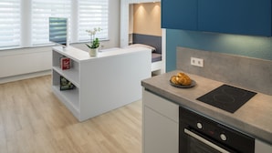 A modern kitchen with a built-in island, a black induction cooktop, and a single oven. - Appartments Drei Morgen (Leinfelden-Echterdingen)