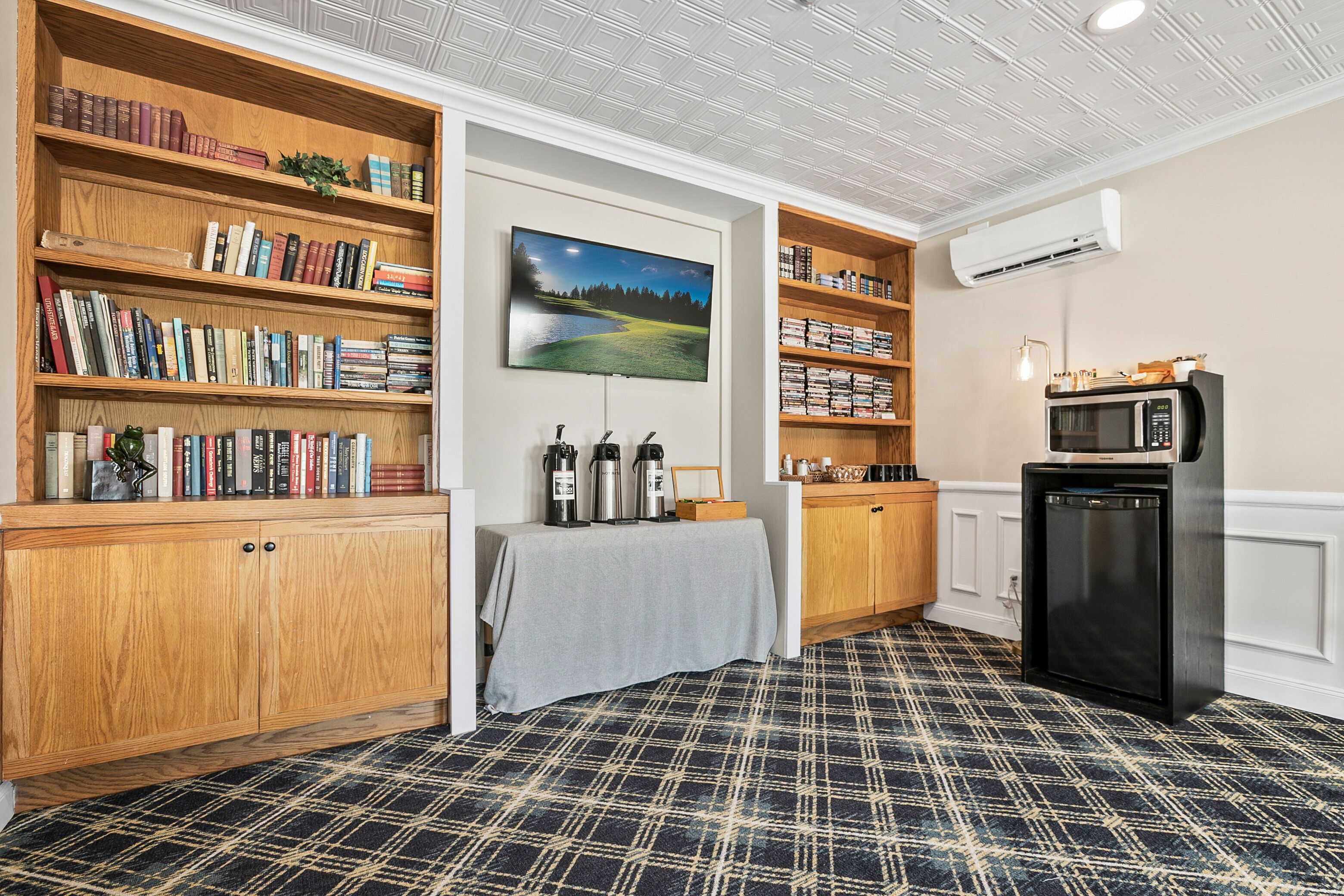 Una habitación acogedora con estanterías de madera, un televisor de pantalla plana, una zona de café y una kitchenette.