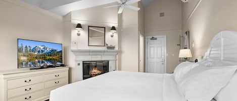 A bedroom with a large bed, a television, a fireplace, and a ceiling fan.
