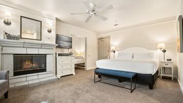 A bedroom with a fireplace, a bed, a bench, a TV, and a ceiling fan.