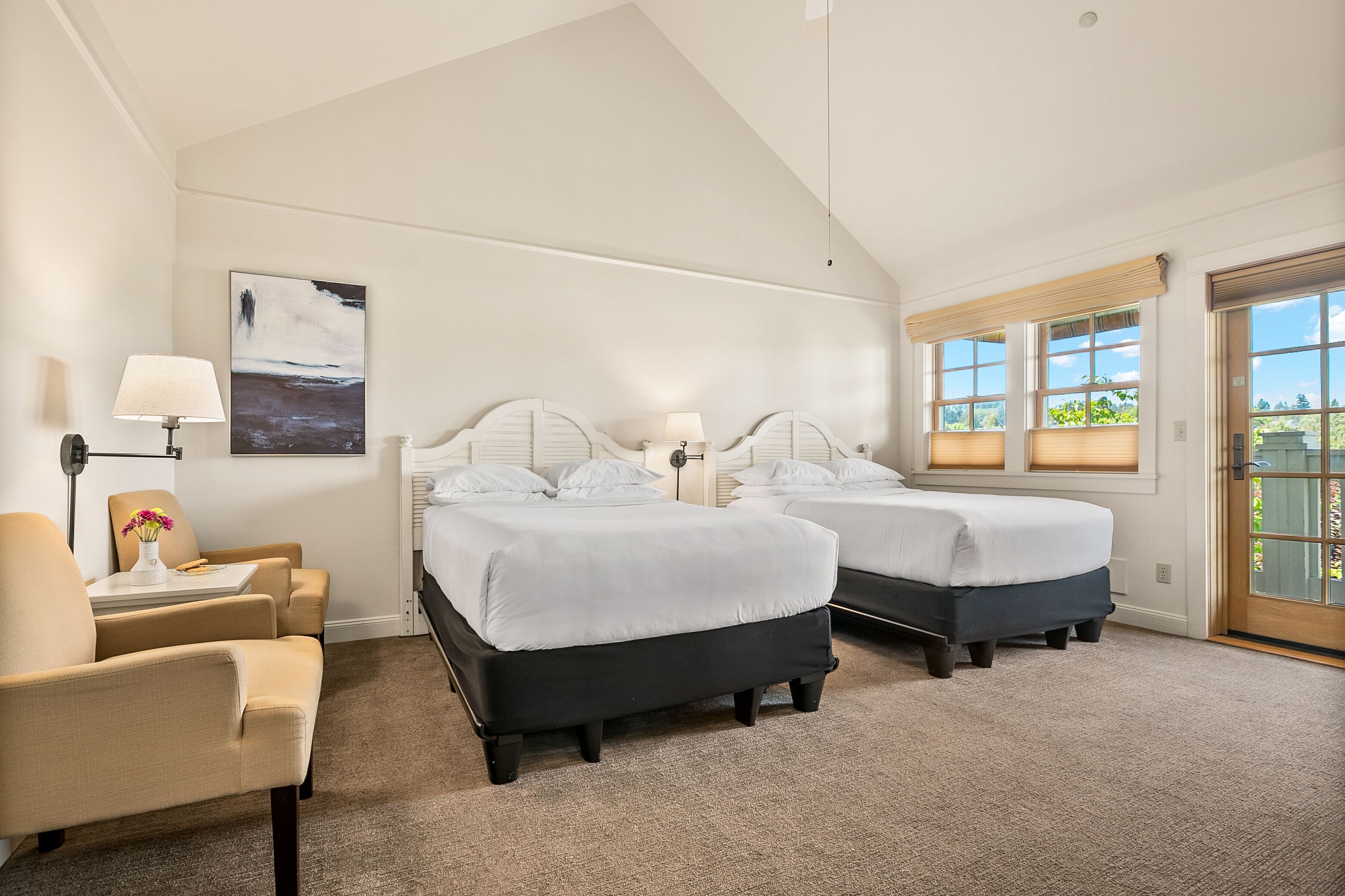 Une chambre d’hôtel avec deux lits, une chaise, une lampe, un tableau et une vue sur l’extérieur.