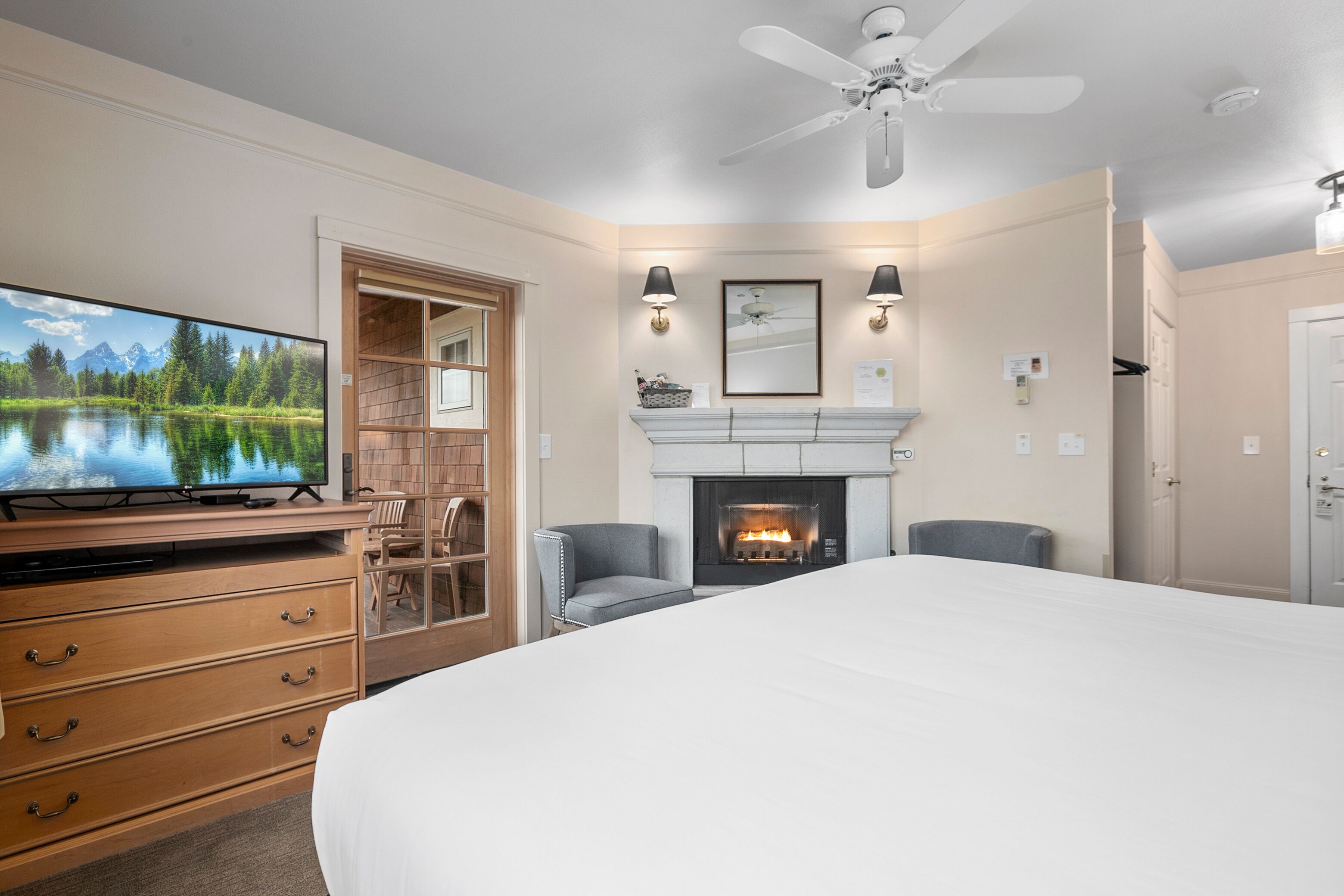 A bedroom with a large bed, a television, a fireplace, and a ceiling fan.
