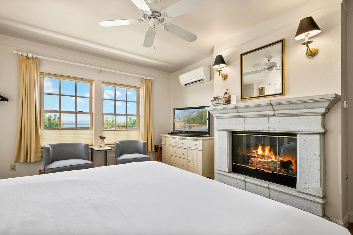 Una habitación de hotel con una cama, dos sillones, un televisor, una chimenea y un ventilador de techo.