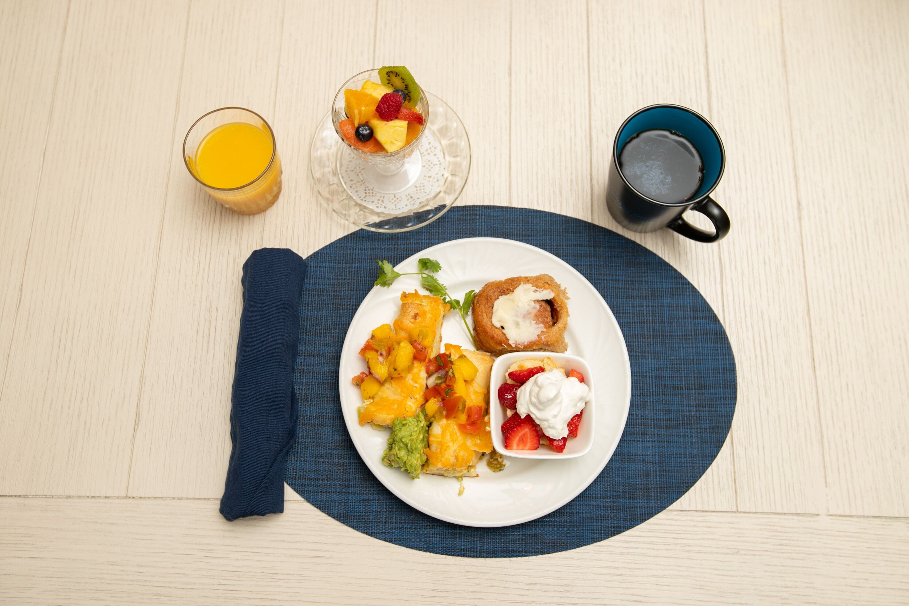 A breakfast setting with a plate of food, a glass of orange juice, and a coffee mug on a wooden table.