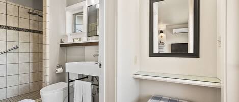A bathroom with a shower, toilet, sink, and a glass shelf.