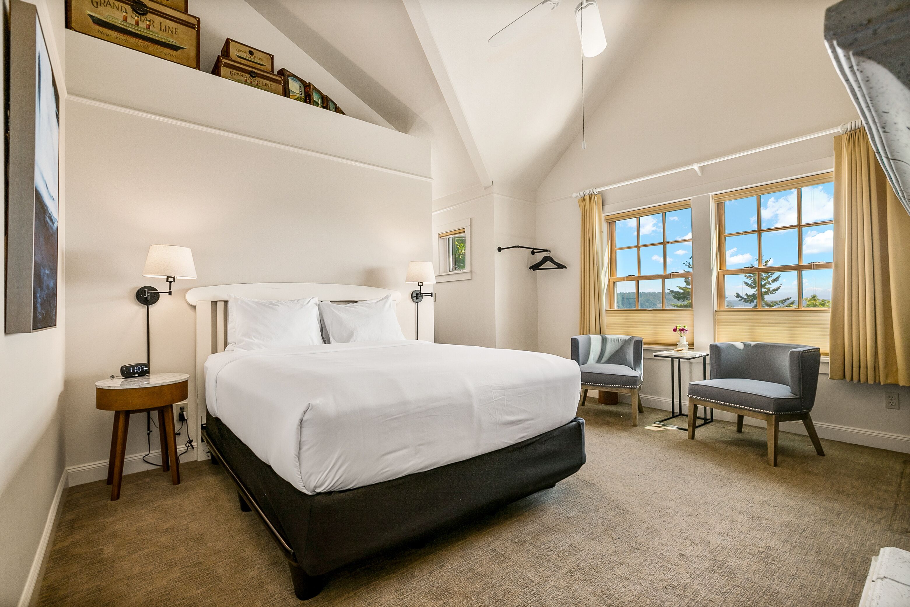A hotel room with a large bed, bedside tables, a chair, a small table, and a window with curtains.