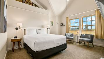 A hotel room with a large bed, bedside tables, a chair, a small table, and a window with curtains.