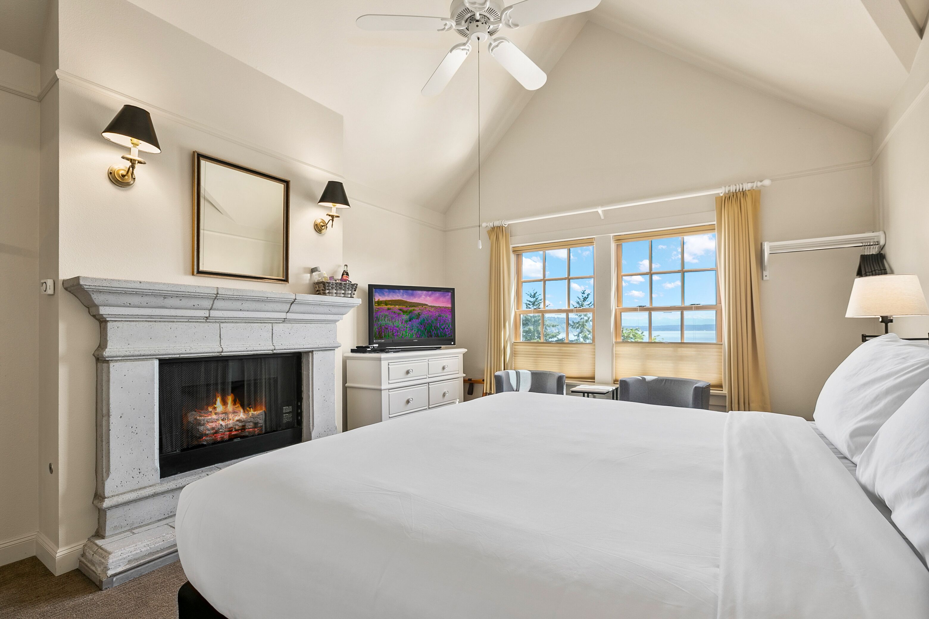 A hotel room with a large bed, a fireplace, a television, and a view of the outdoors.
