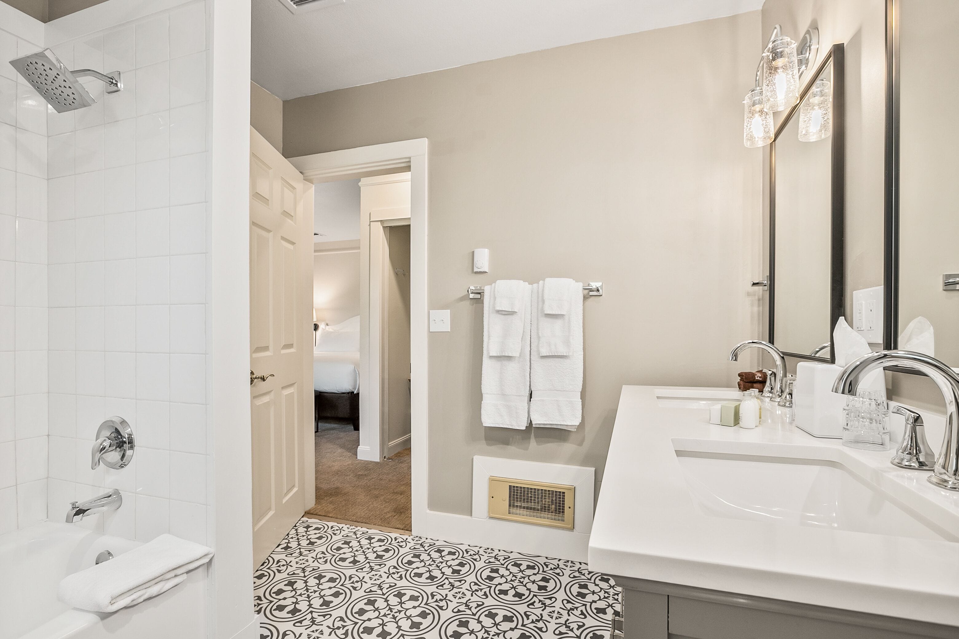 A modern bathroom with a shower, two sinks, a large mirror, and a patterned floor.