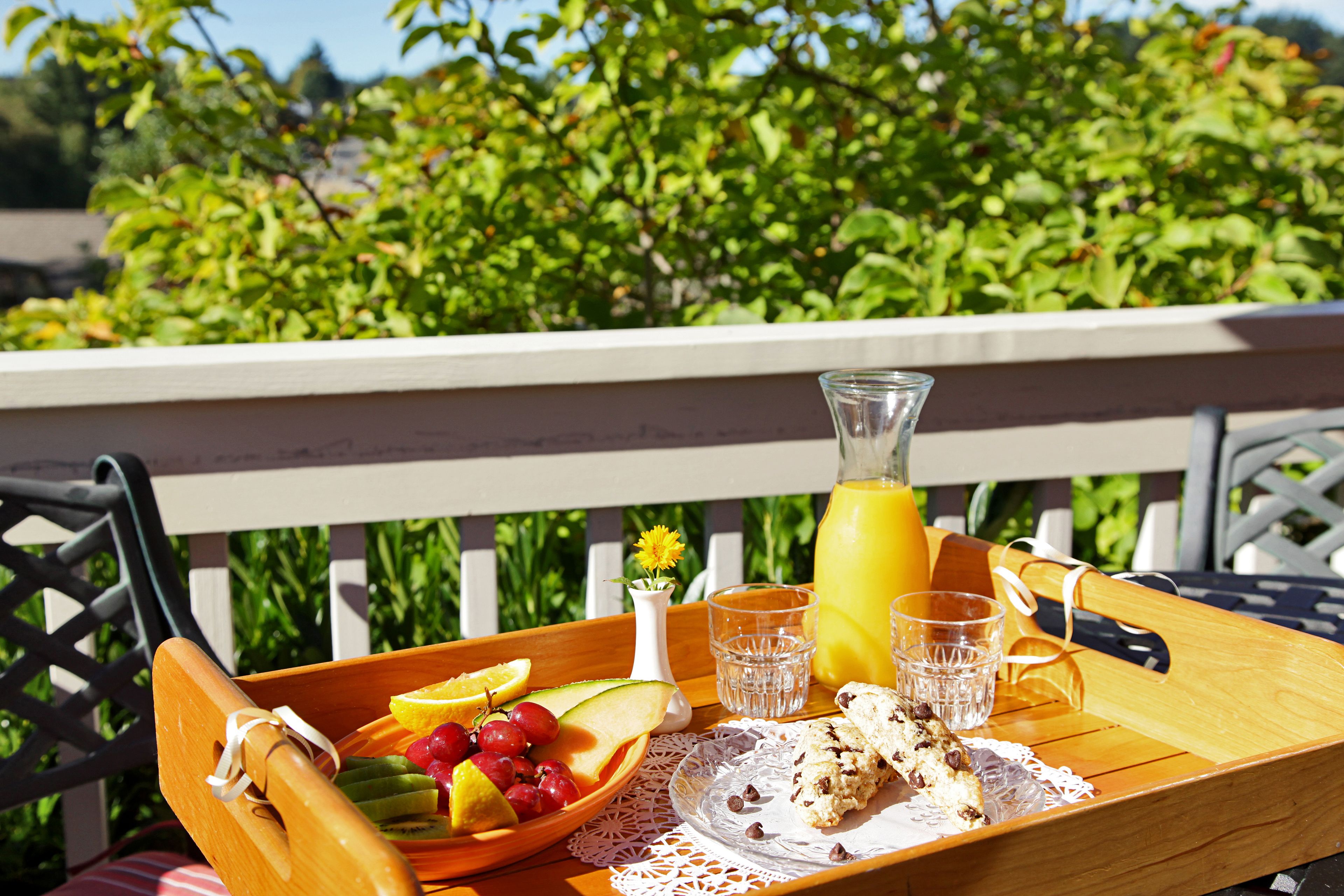 A wooden tray with fruits, cookies, and a glass of orange juice on an outdoor table.