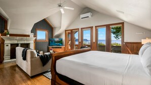 Une chambre avec un grand lit, un ventilateur de plafond, une cheminée, une télévision et une vue sur l’océan.