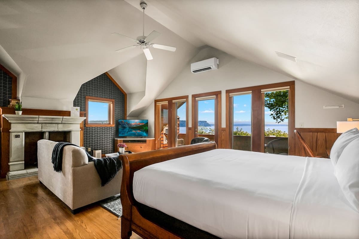 Un dormitorio con una cama grande, ventilador de techo, chimenea, televisor y vista al océano.