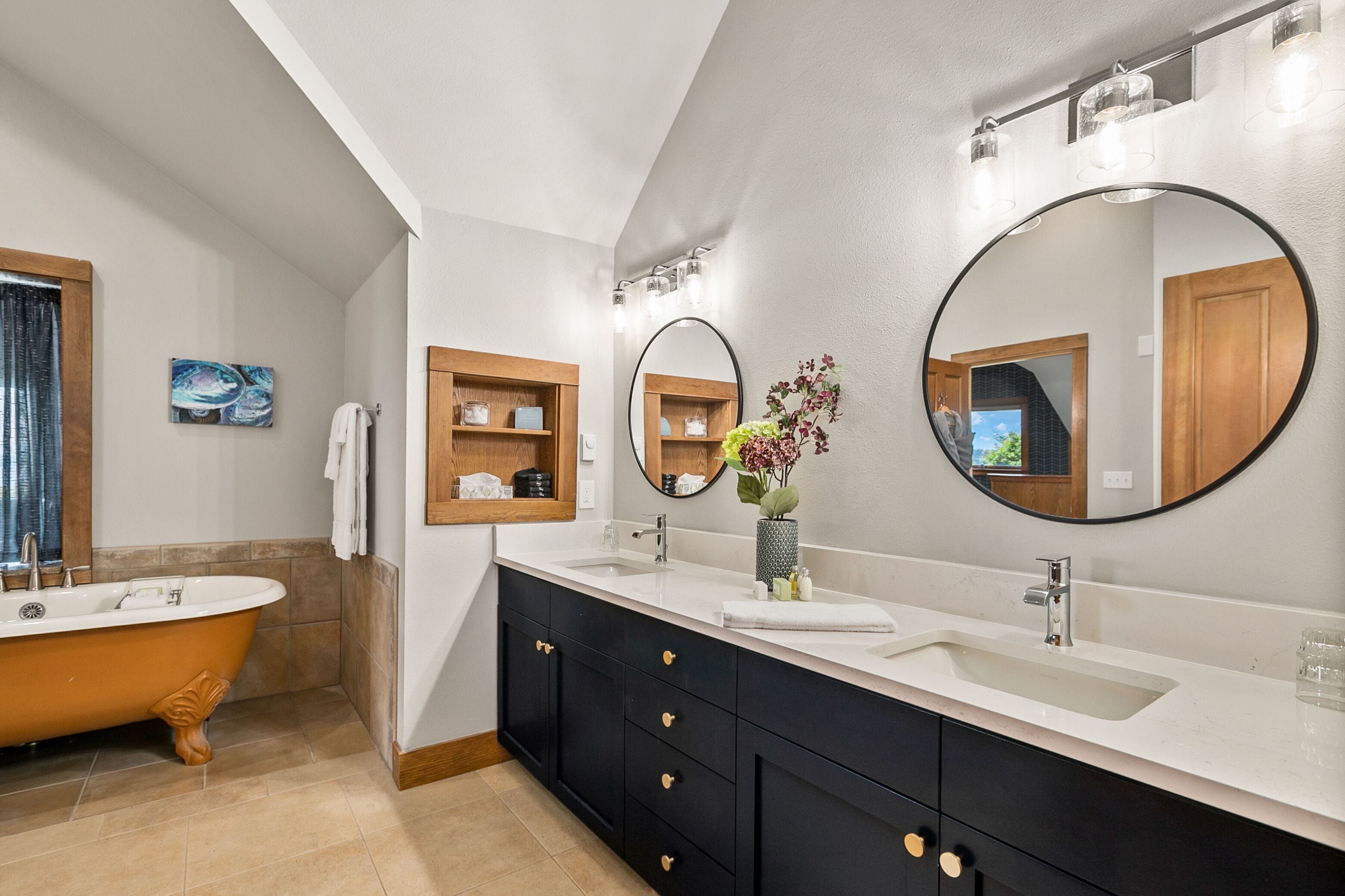 A modern bathroom with a freestanding bathtub, a vanity with a large mirror, and built-in shelves.