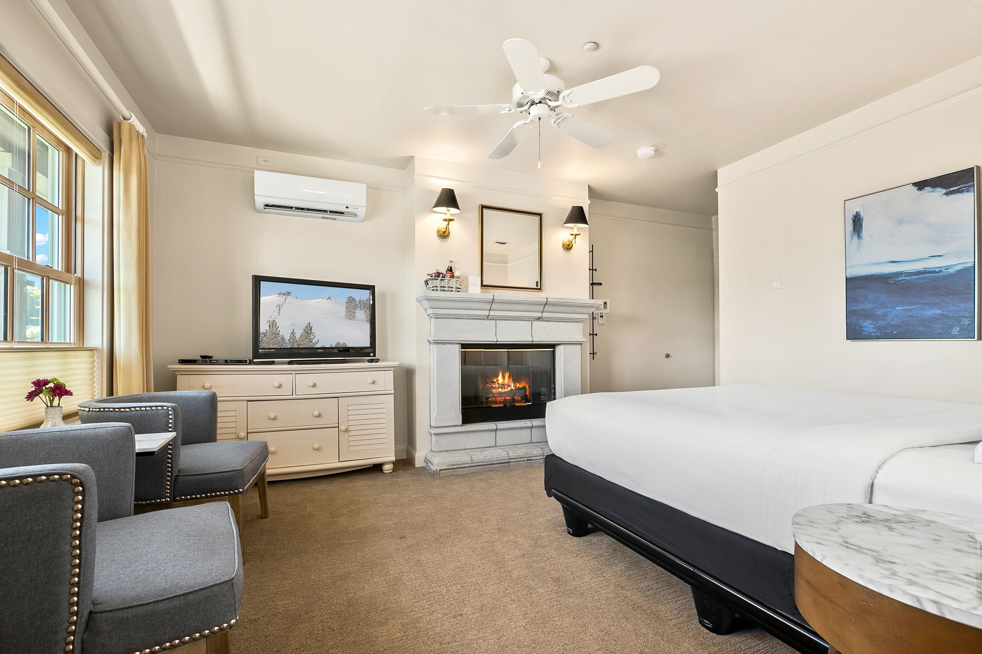 A hotel room with a large bed, a fireplace, a television, and a ceiling fan.