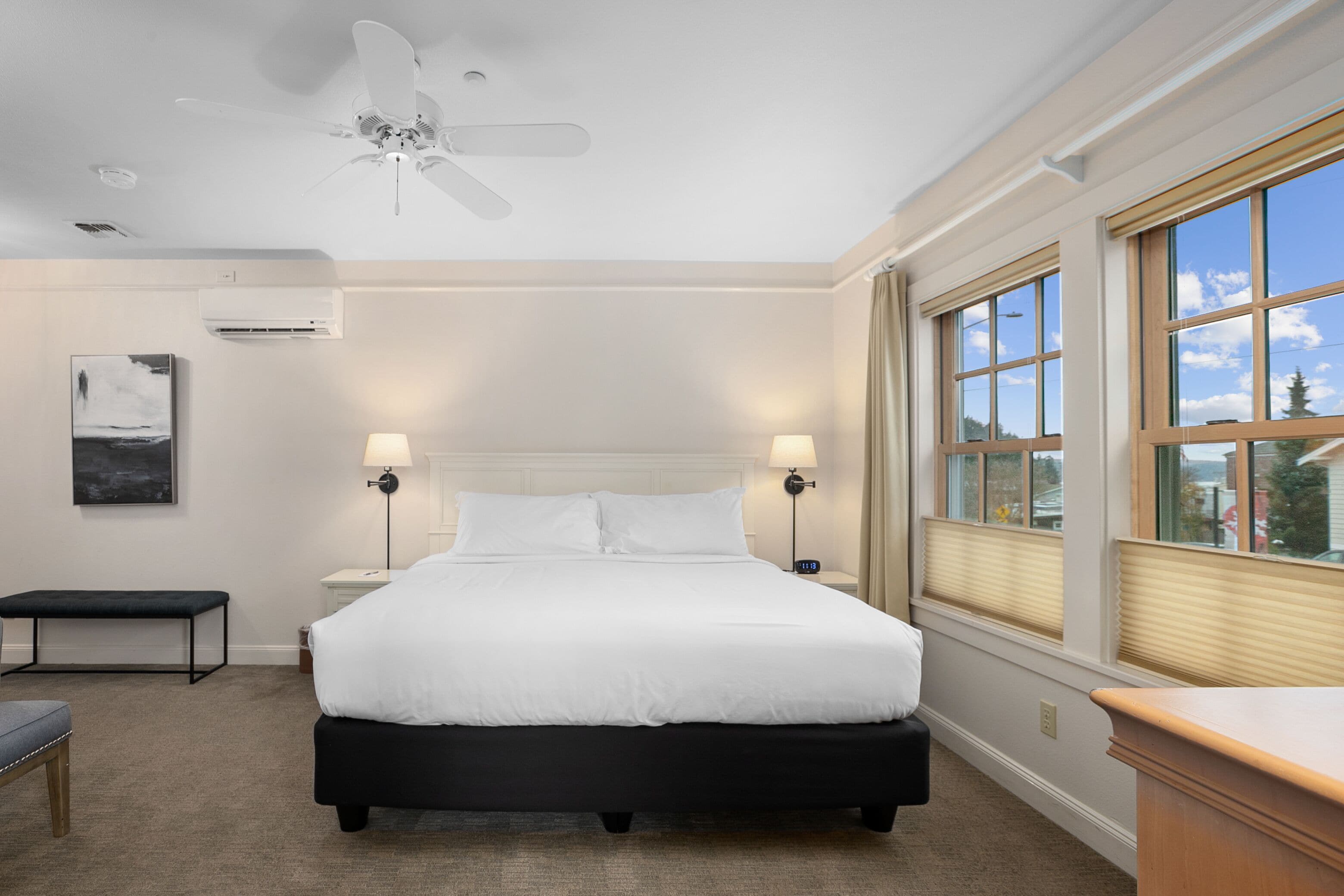 Une chambre à coucher bien aménagée, avec un grand lit, des lampes de chevet, un ventilateur de plafond et une fenêtre équipée de stores.