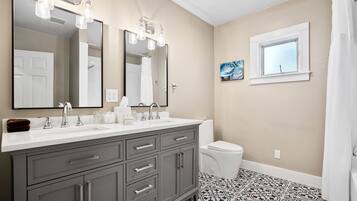 A bathroom with a double sink vanity, a toilet, a window, and a shower curtain.