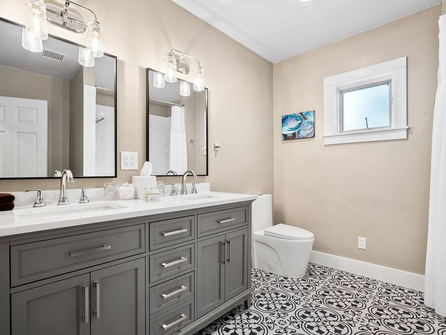 A bathroom with a double sink vanity, a toilet, a window, and a shower curtain.