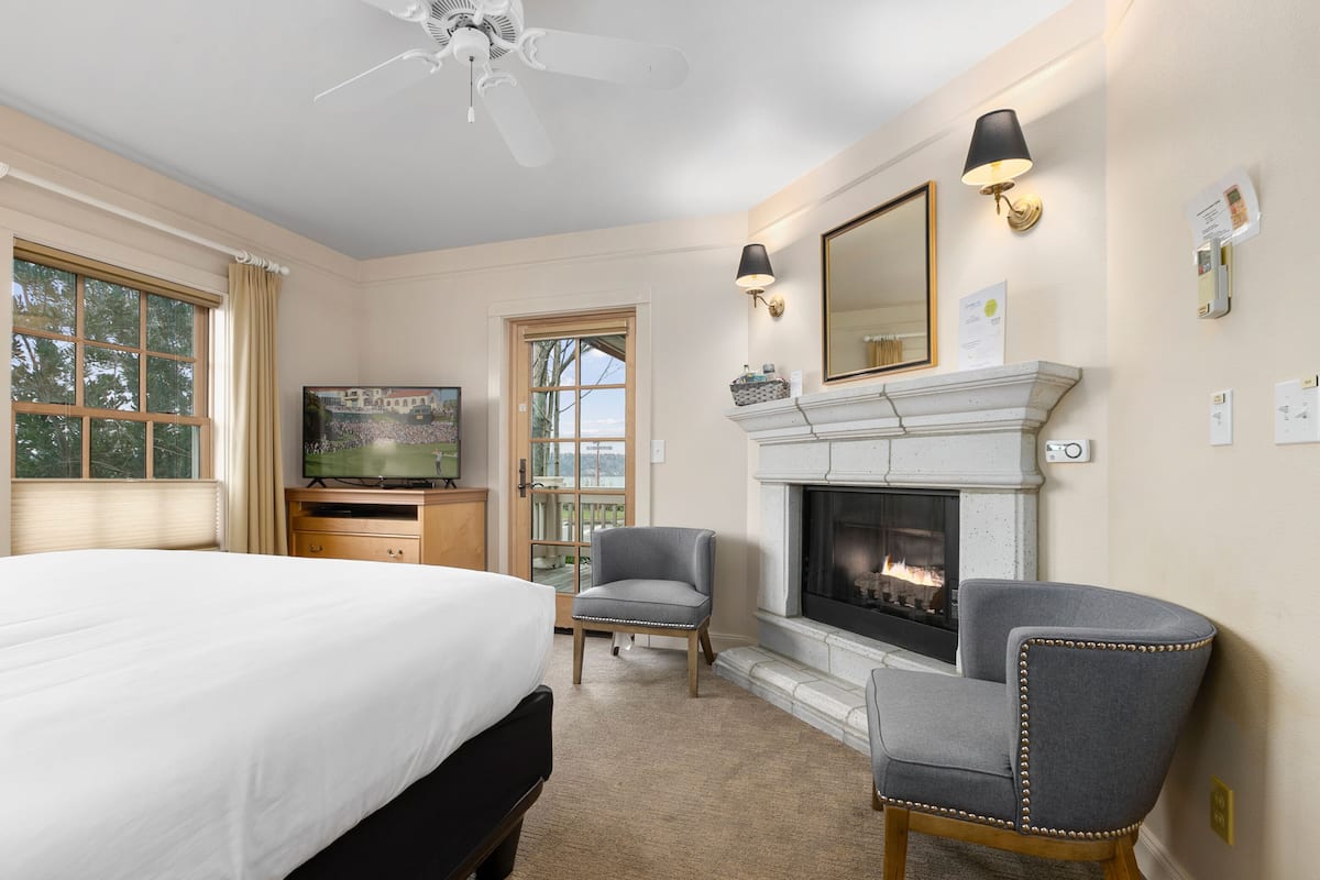 Una habitación de hotel con una cama grande, televisión, chimenea y dos sillones.