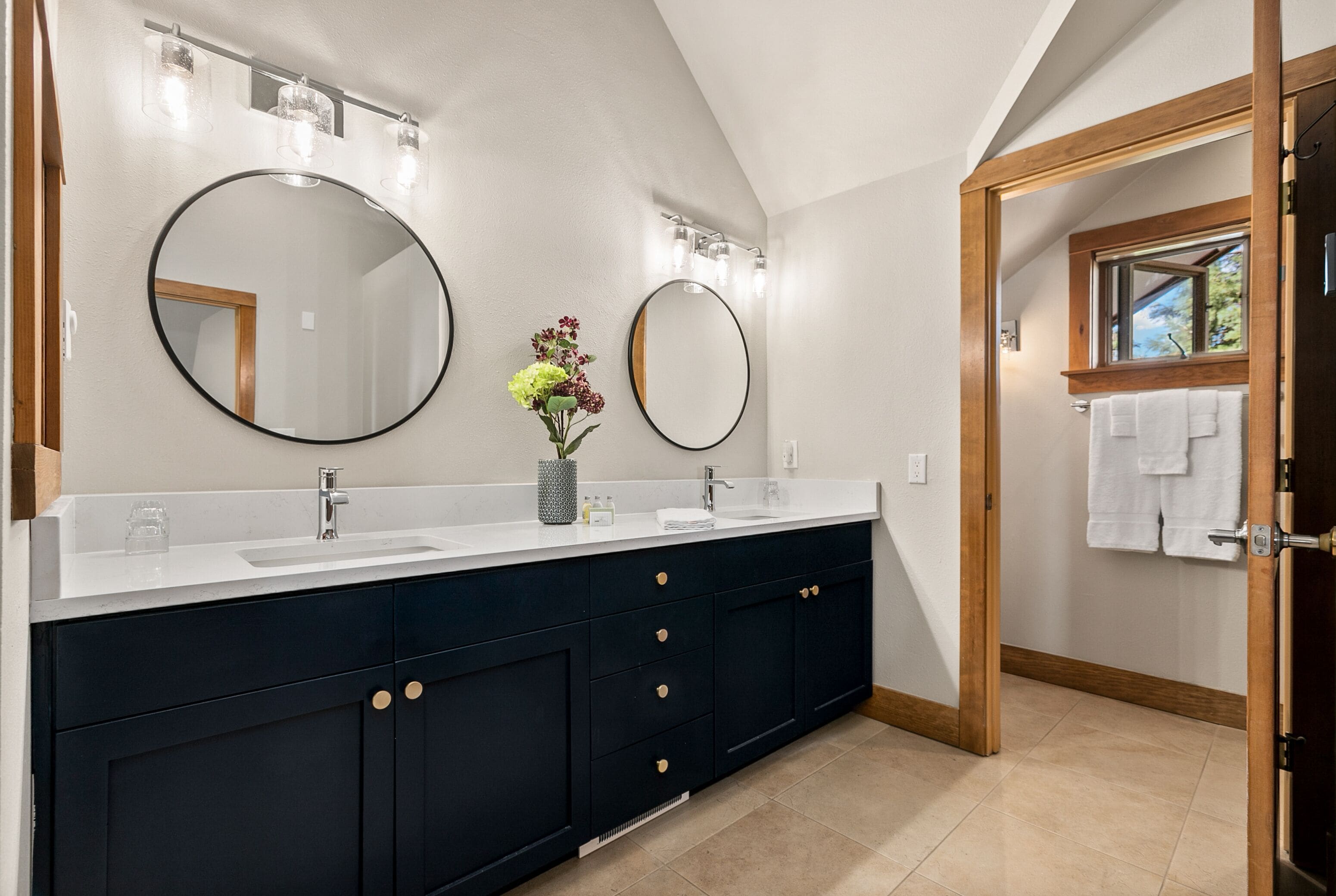 Un baño moderno con un tocador oscuro, dos espejos redondos y una encimera blanca.