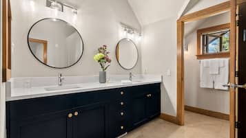 Un baño moderno con un tocador oscuro, dos espejos redondos y una encimera blanca.