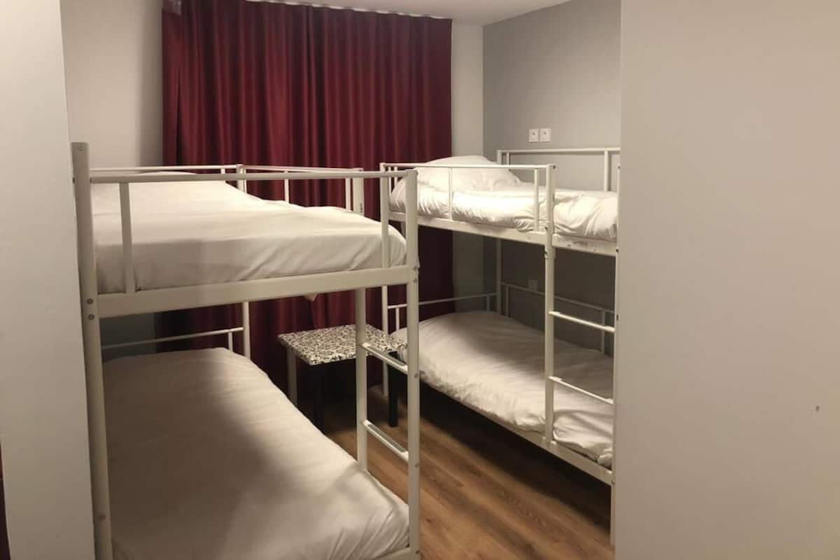 Une chambre avec un lit superposé, un plancher en bois, un rideau rouge et un plafonnier blanc.