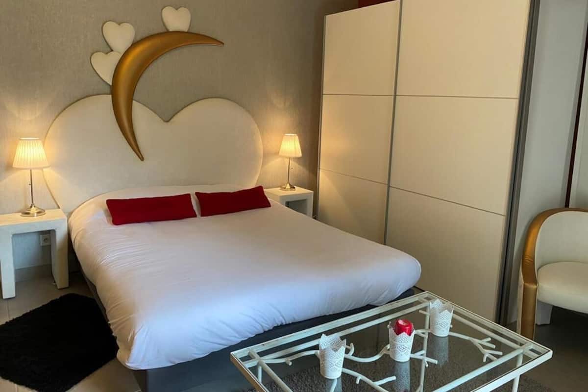 Une chambre d’hôtel avec un grand lit, deux lampes de chevet, une table basse en verre et une armoire.