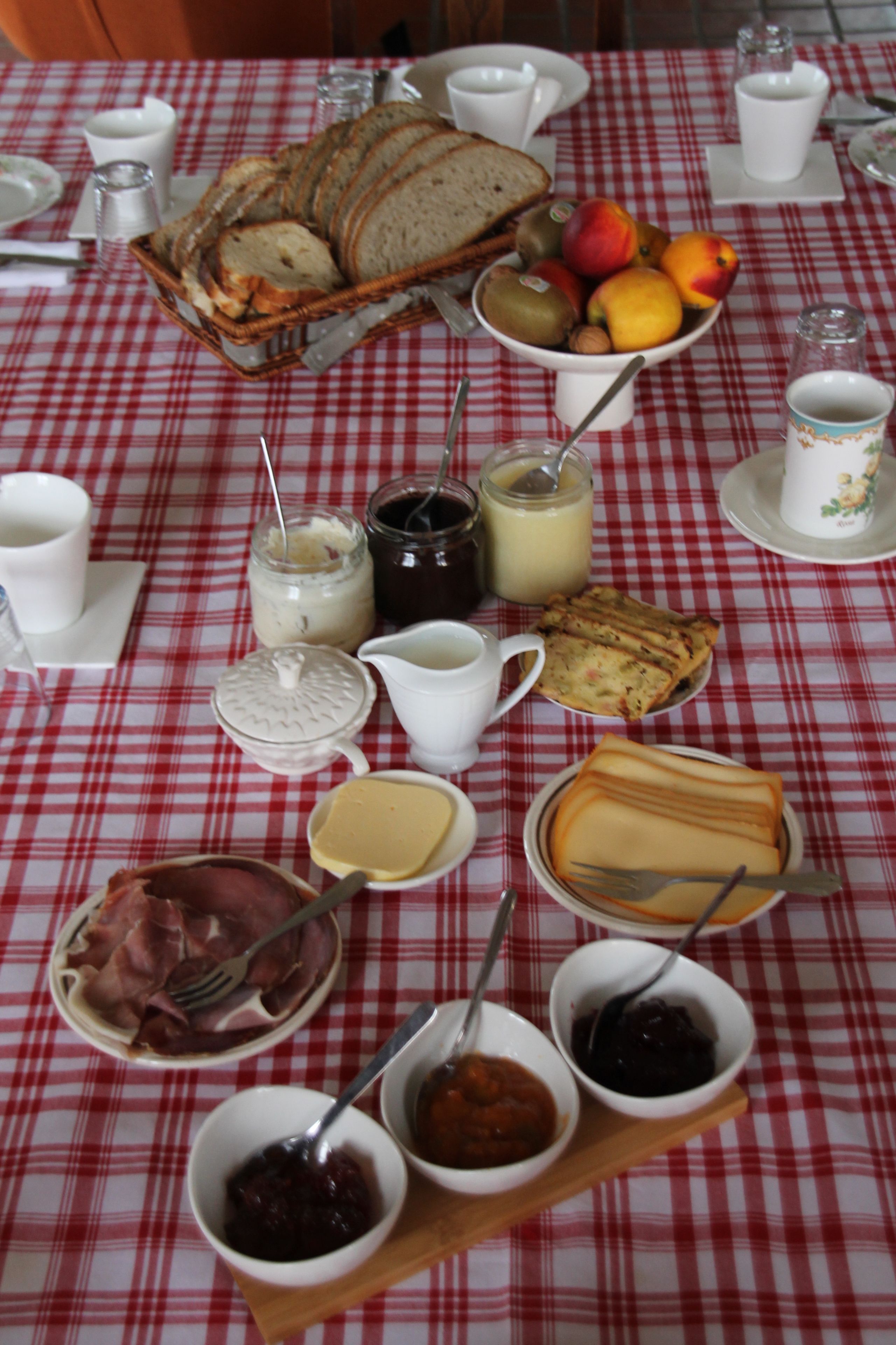 A table set with various food items including bread, fruits, cheeses, and condiments.