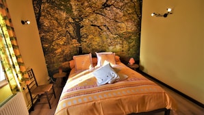 Een slaapkamer met een grote muurschildering van een boom, een bed met oranje beddengoed, een stoel en een kleine tafel.