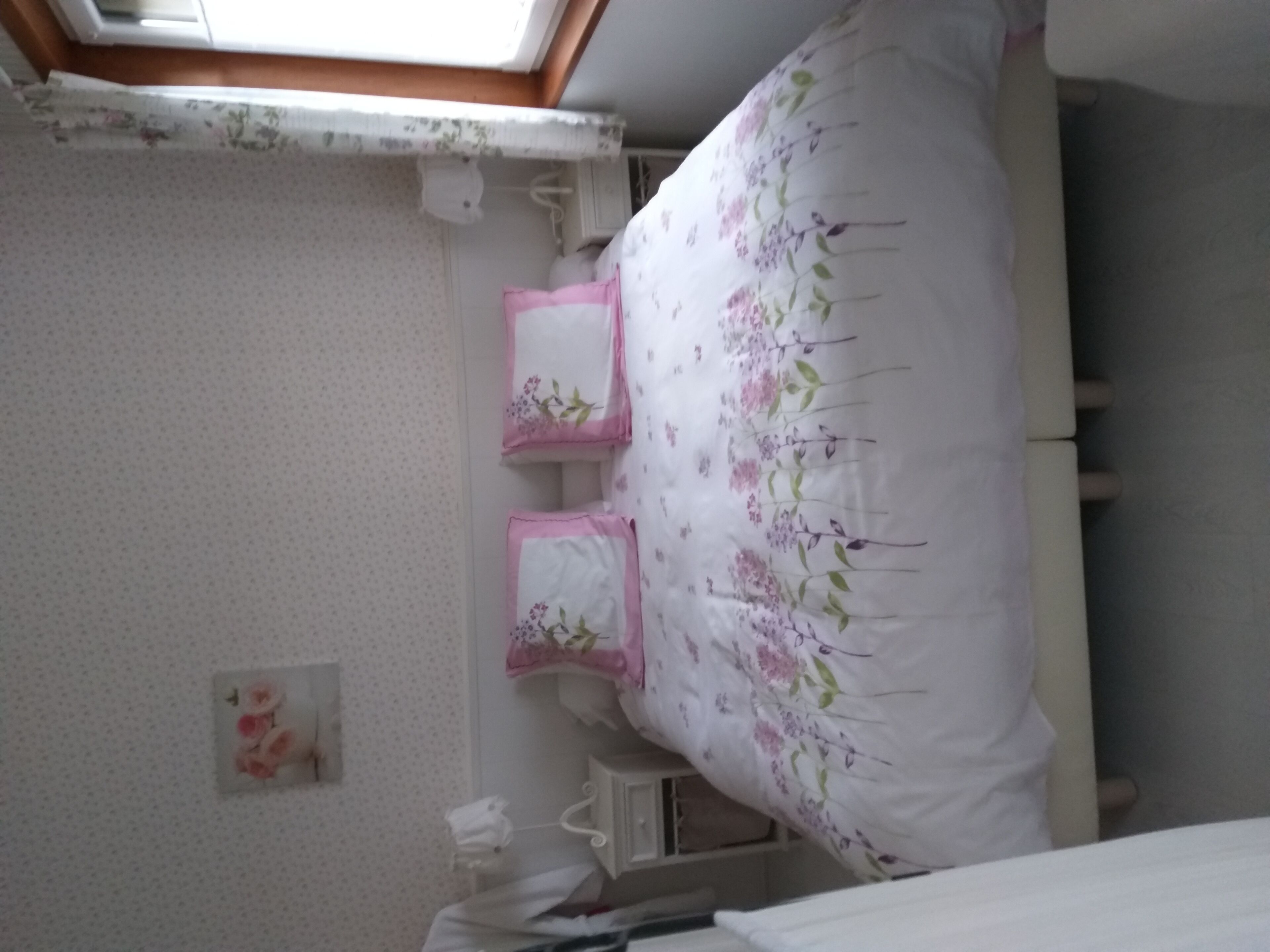 A bedroom with a bed, a bedside table, a nightstand, and a wall-mounted shelf.