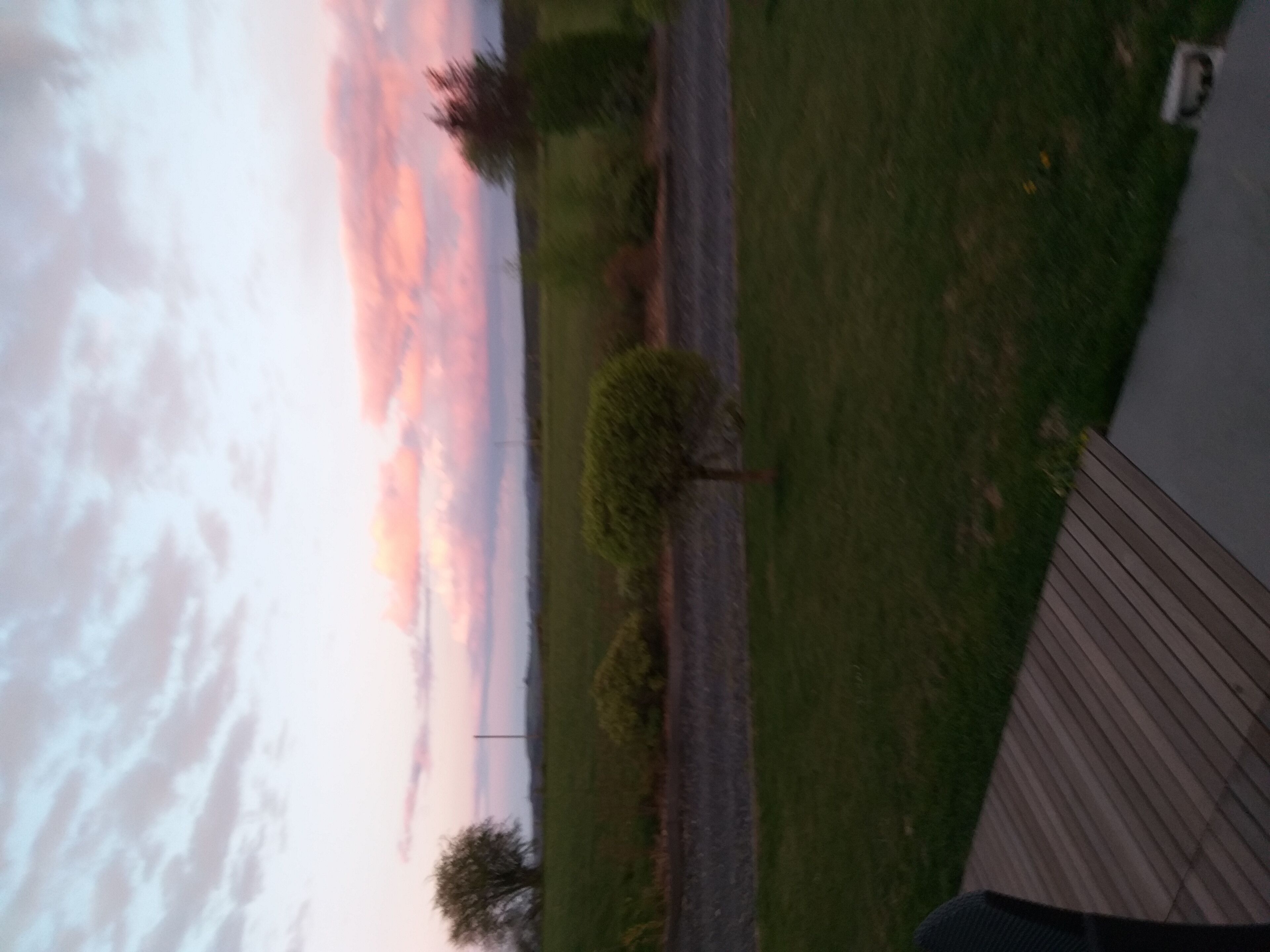 Une vue d’un coucher de soleil sur une zone herbeuse, avec une terrasse en bois et un bâtiment au premier plan.