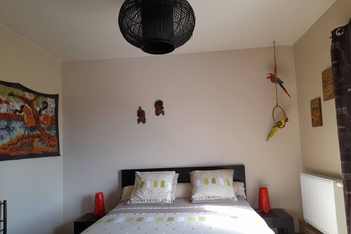 Ein Schlafzimmer mit einem Bett, zwei Nachttischen, einer Pendelleuchte, einem Wandbild und einer Heizung.