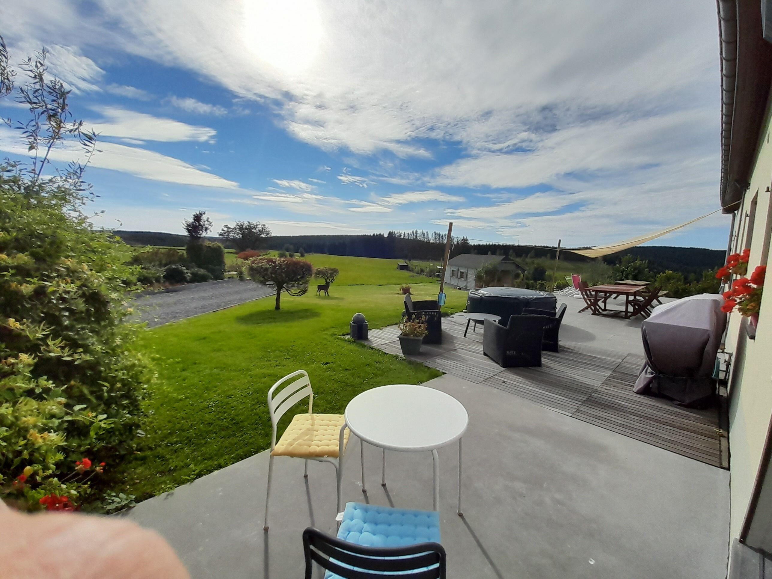 Un patio con mobiliario exterior, una parrilla y vistas a un paisaje verde con árboles y una colina distante.