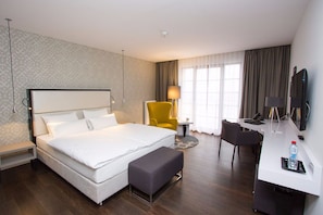 A hotel room with a large bed, a desk with a chair, a TV, and a lamp. - Hotel Wemperhardt (Weiswampach)