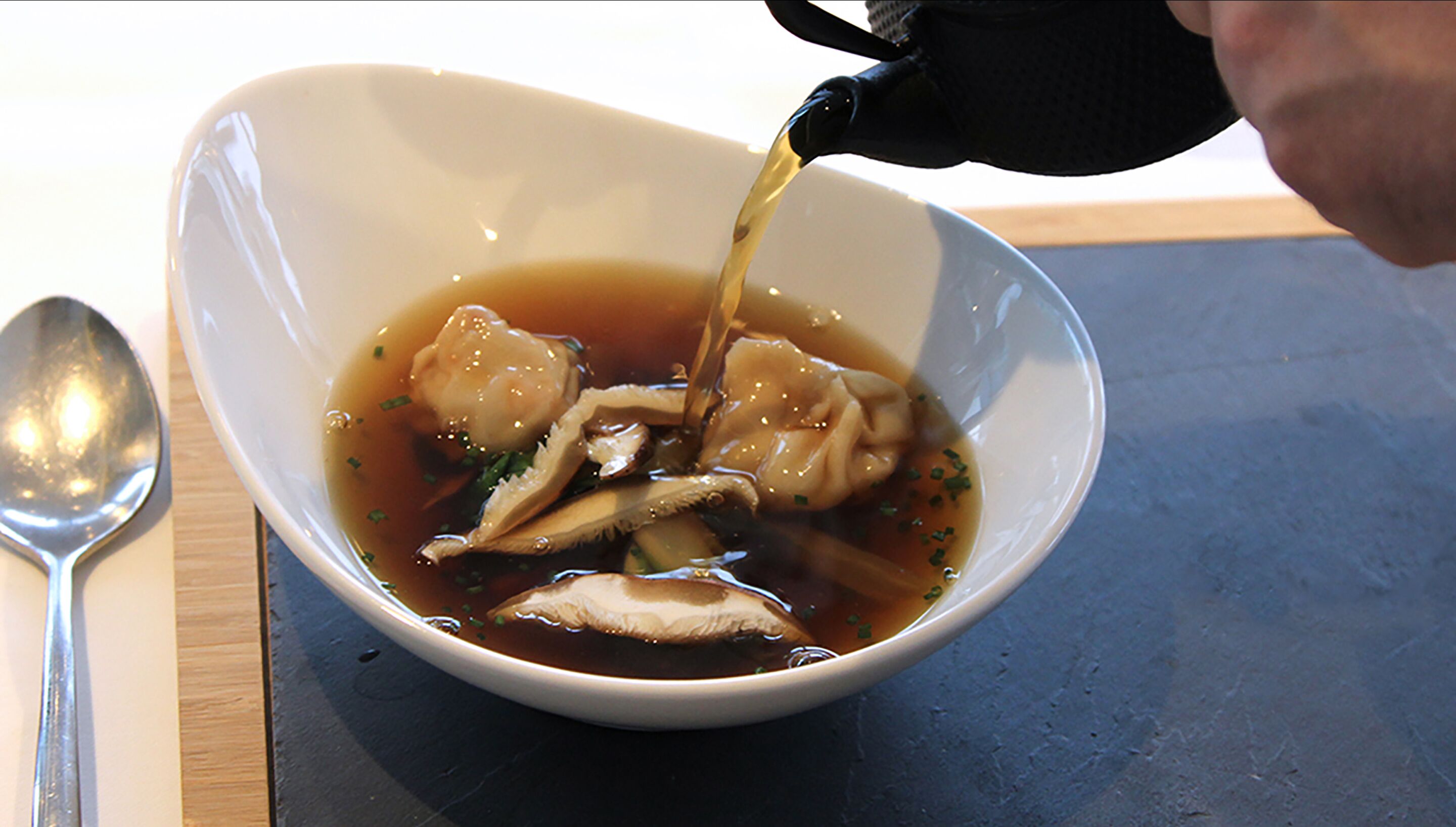 A bowl of soup with dumplings and broth being poured into it.